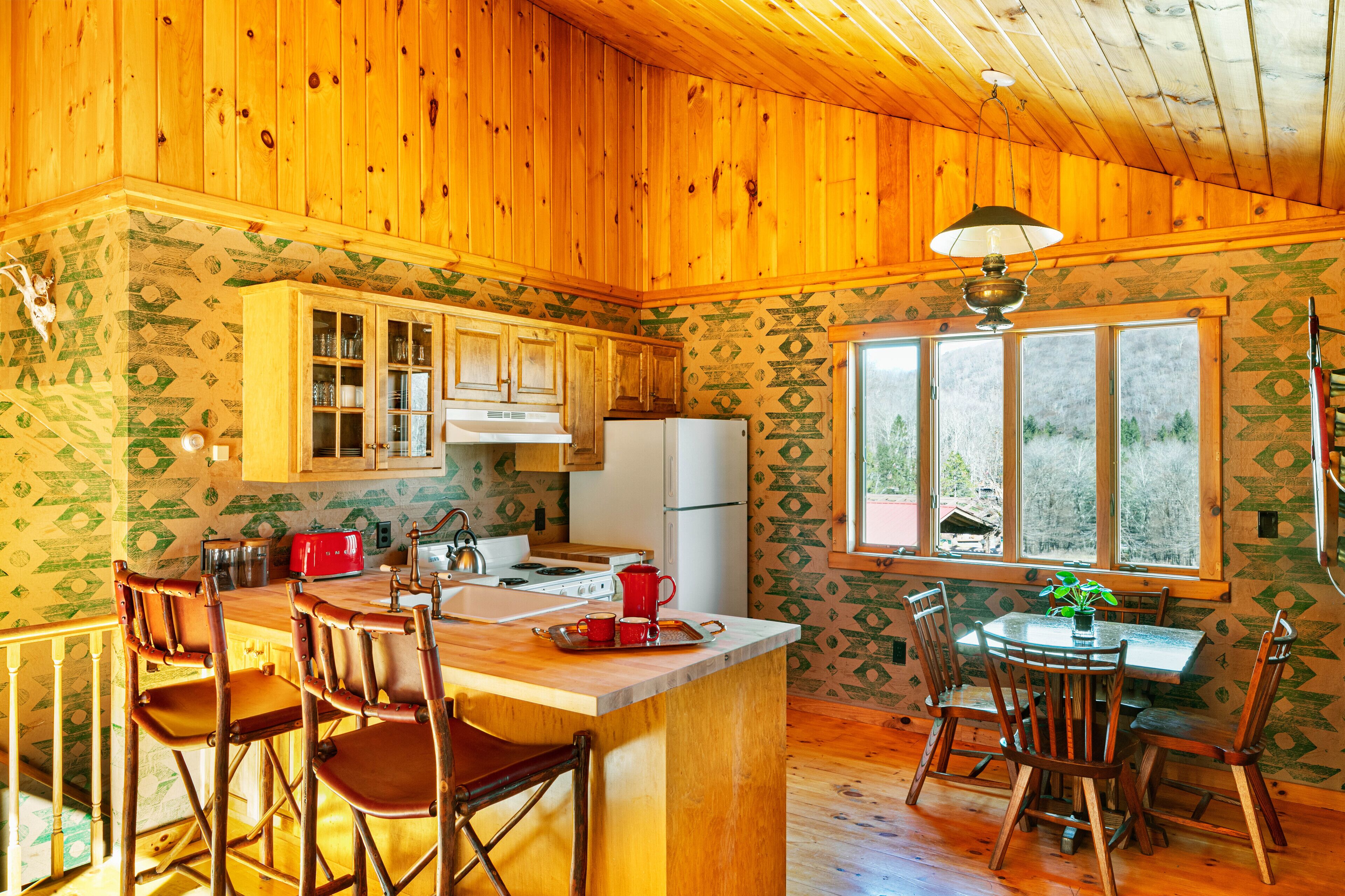 Cocina de cabaña de madera con una isla central, taburetes de bar y una mesa de comedor con sillas.