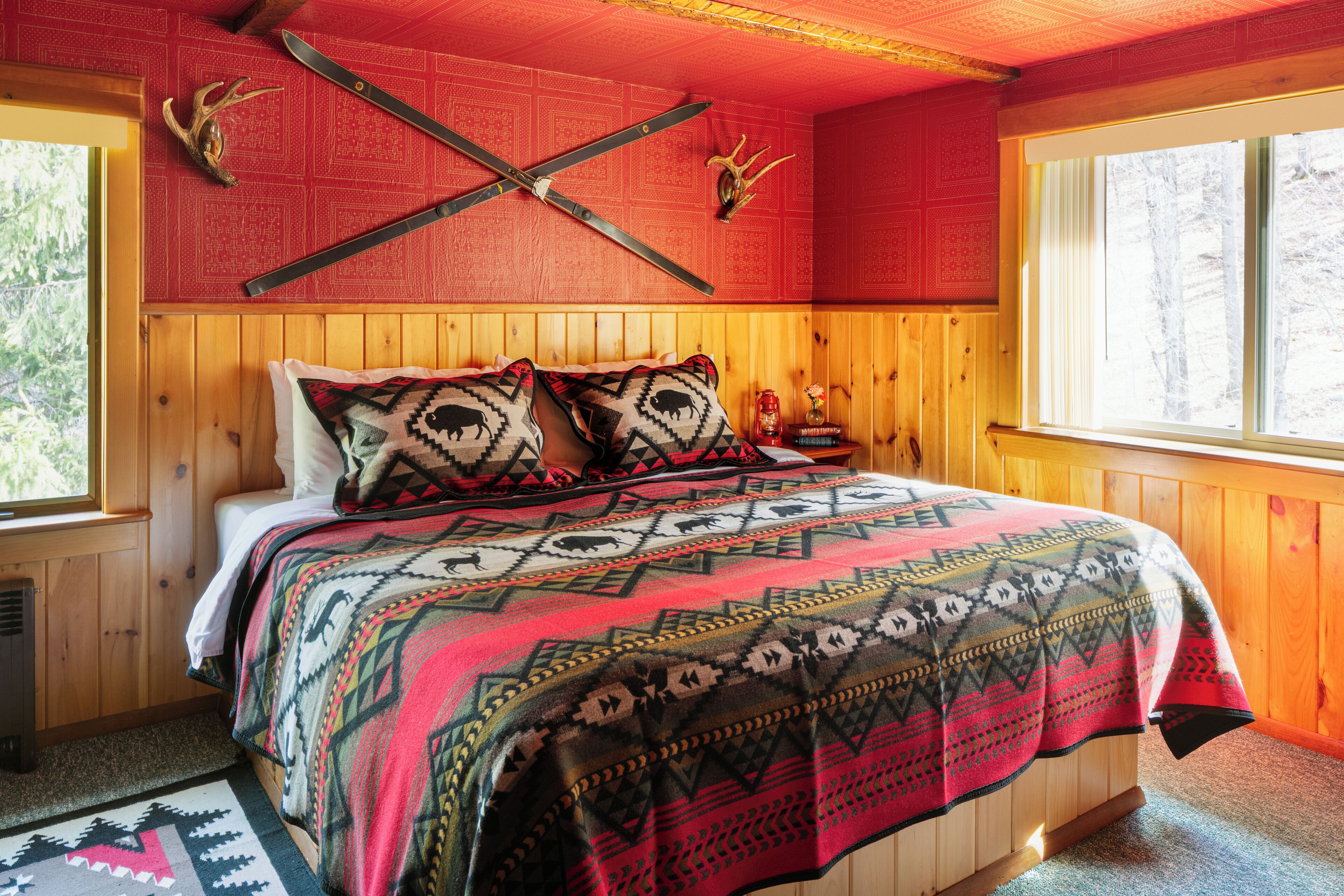 A wooden cabin room with a bed, a window, and two antlers on the wall.