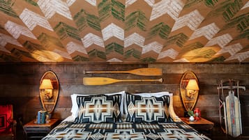 A room with a patterned ceiling, wooden walls, a bed with patterned bedding, two wall-mounted lamps, and a wooden bat on the wall.