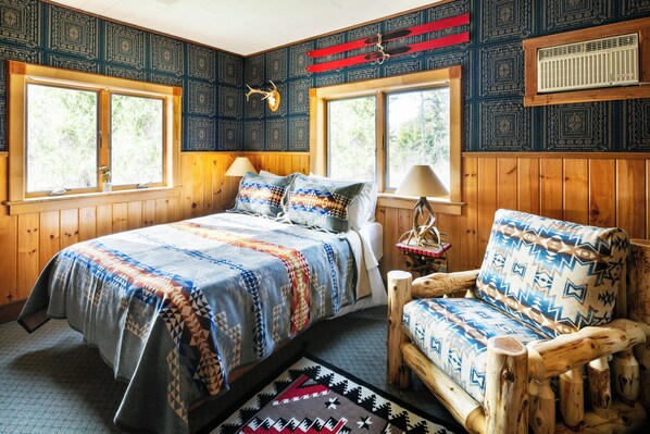 Una habitación acogedora con una cama, una silla de madera y una ventana con vistas a árboles.