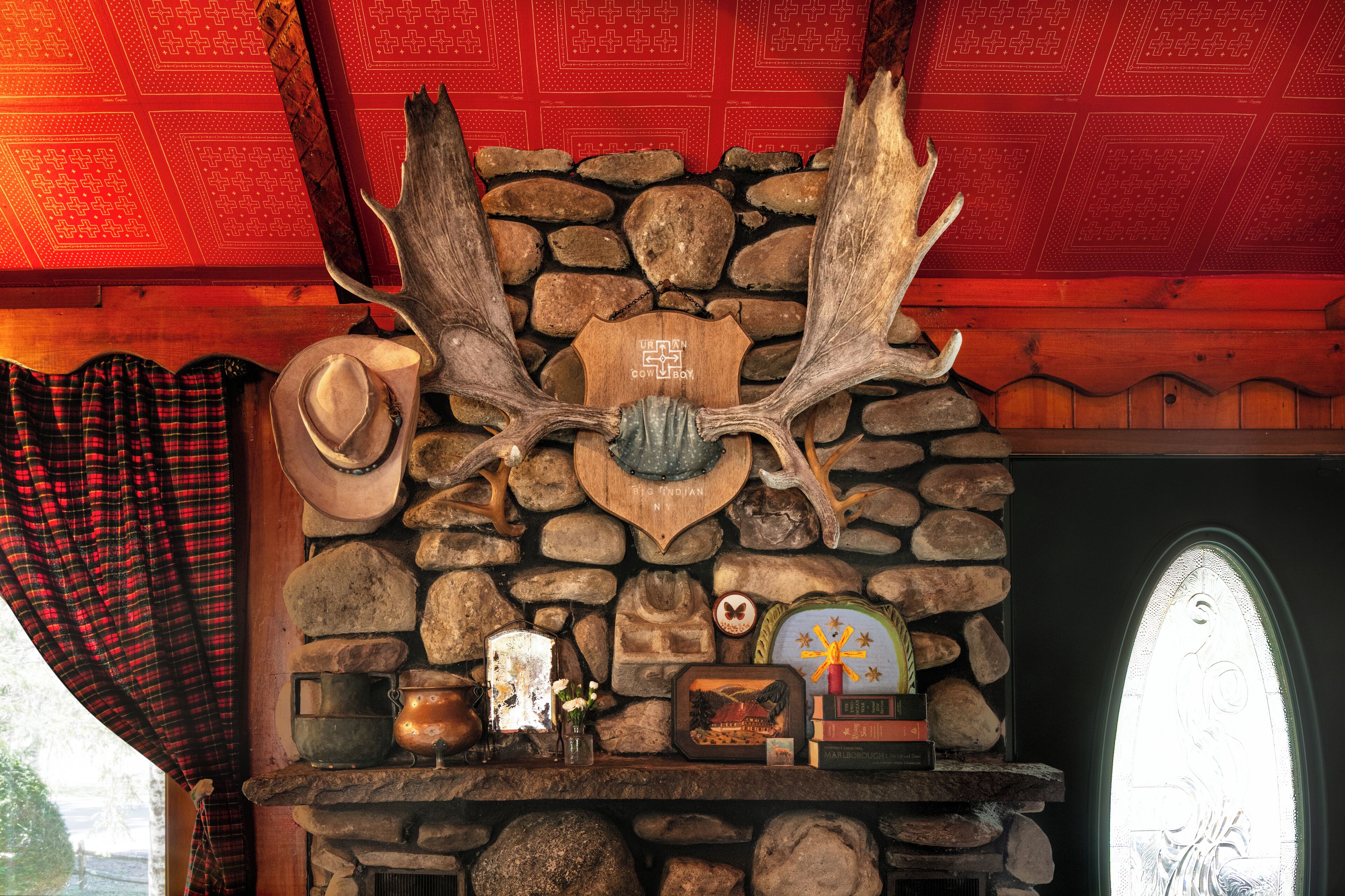 A stone fireplace with antlers, a cowboy hat, and a rustic decor including a clock and books.