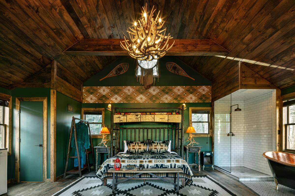 A rustic wooden interior with a large bed, a chandelier, and a bathtub.