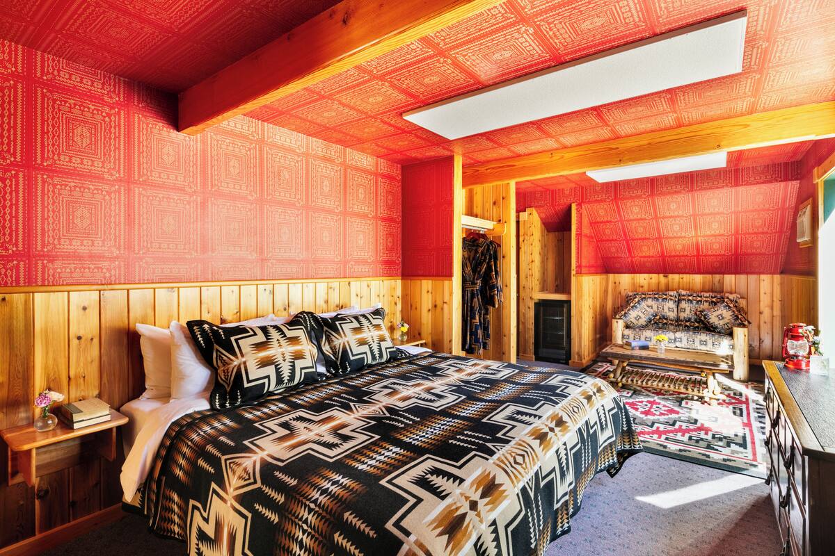 A cozy room with a large bed, wooden walls, and a skylight.