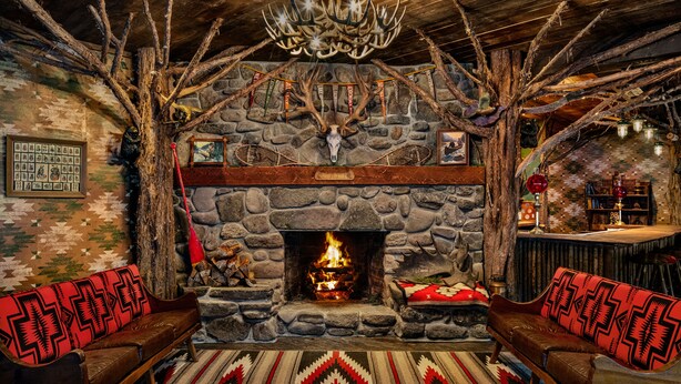 A rustic interior with a stone fireplace, wooden beams, and a chandelier.