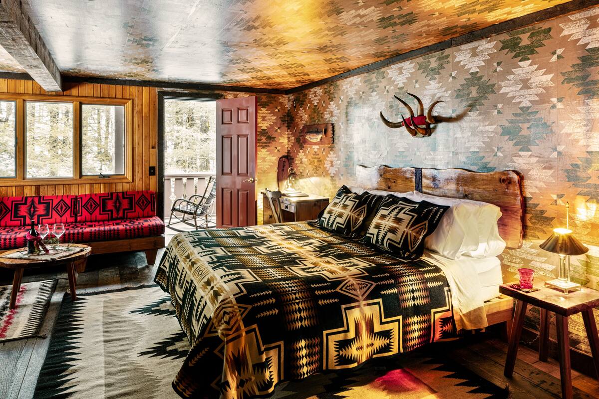 A cozy bedroom with a bed, a wooden bench, a nightstand, and a wall-mounted lamp.