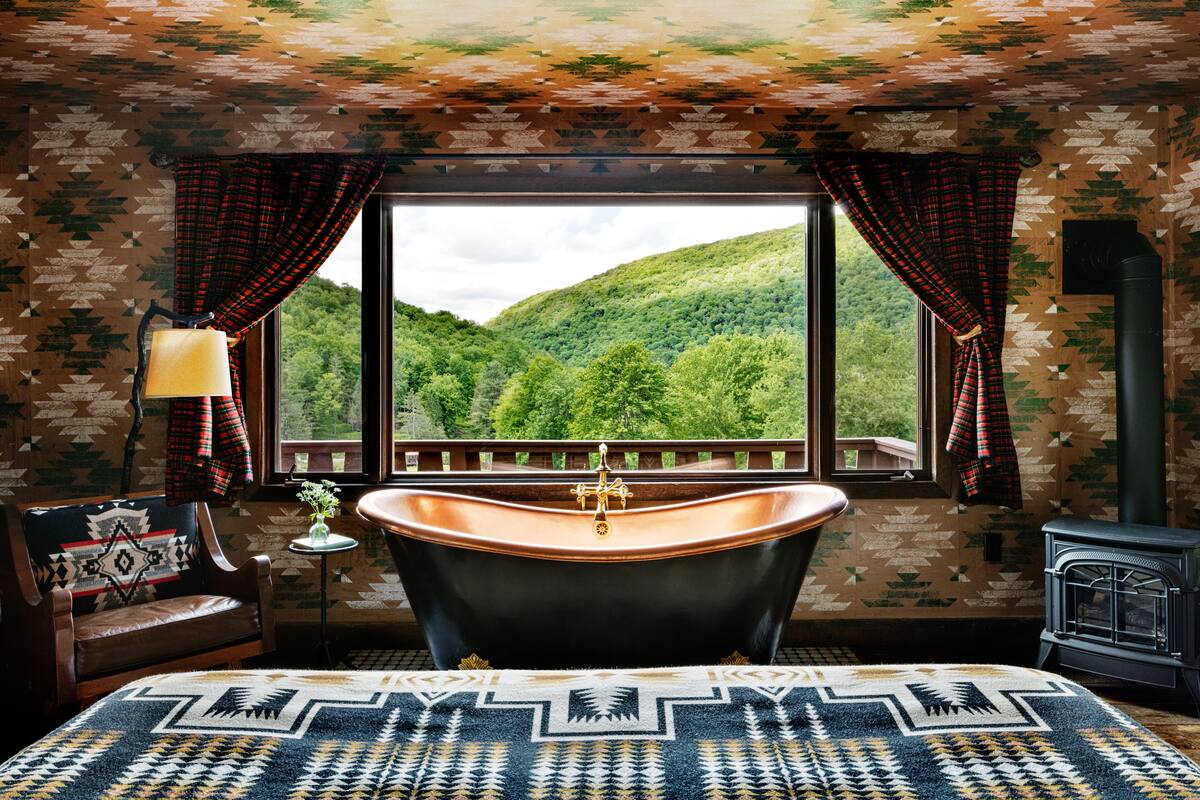 A room with a large window, a bathtub, a chair, a lamp, and a heater.