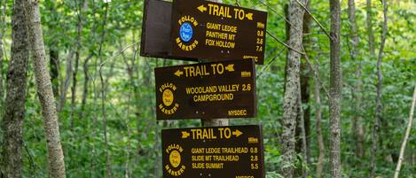 Un letrero de sendero en un bosque con indicaciones a varios destinos para caminatas.