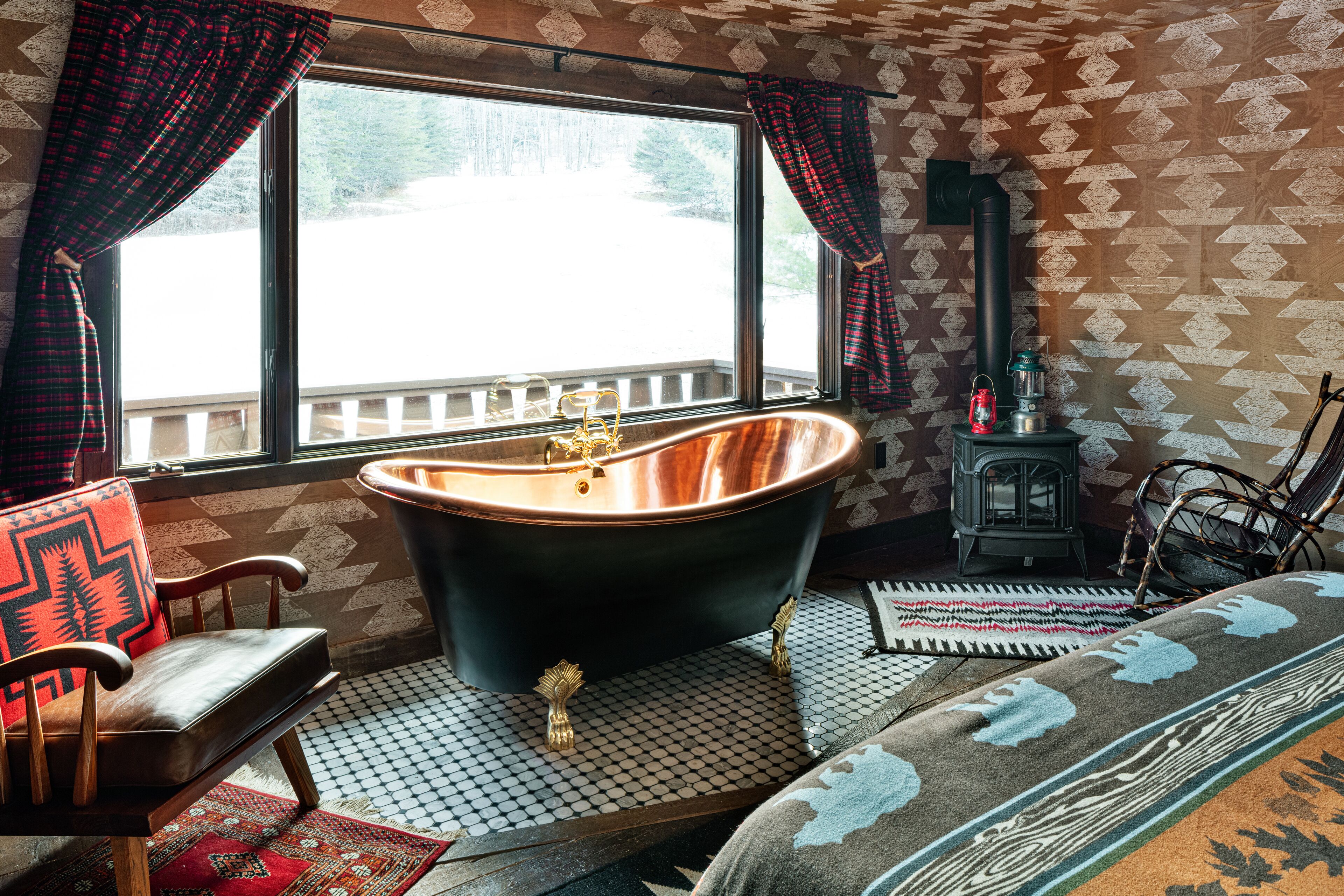 A room with a large window, a black bathtub, a wooden chair, a patterned rug, and a small heater.