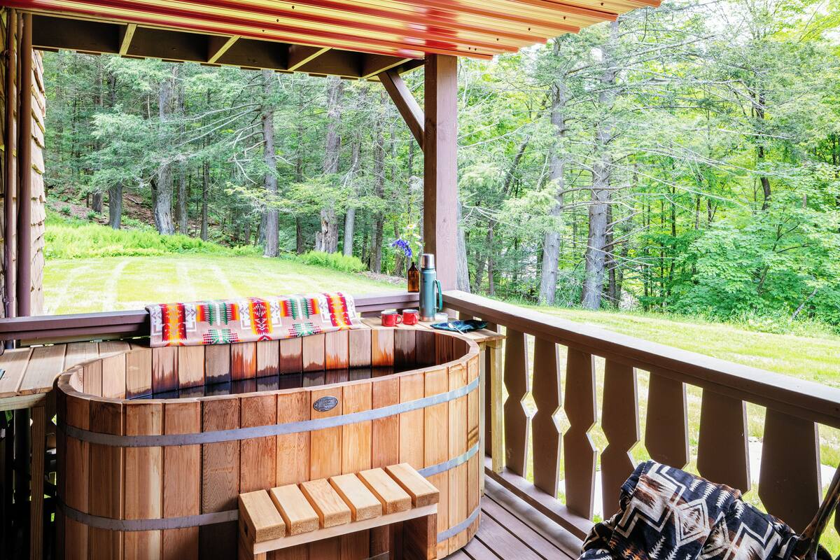 A wooden hot tub on a deck with a view of a forest.