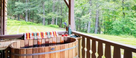 A wooden hot tub on a deck with a view of a forest.