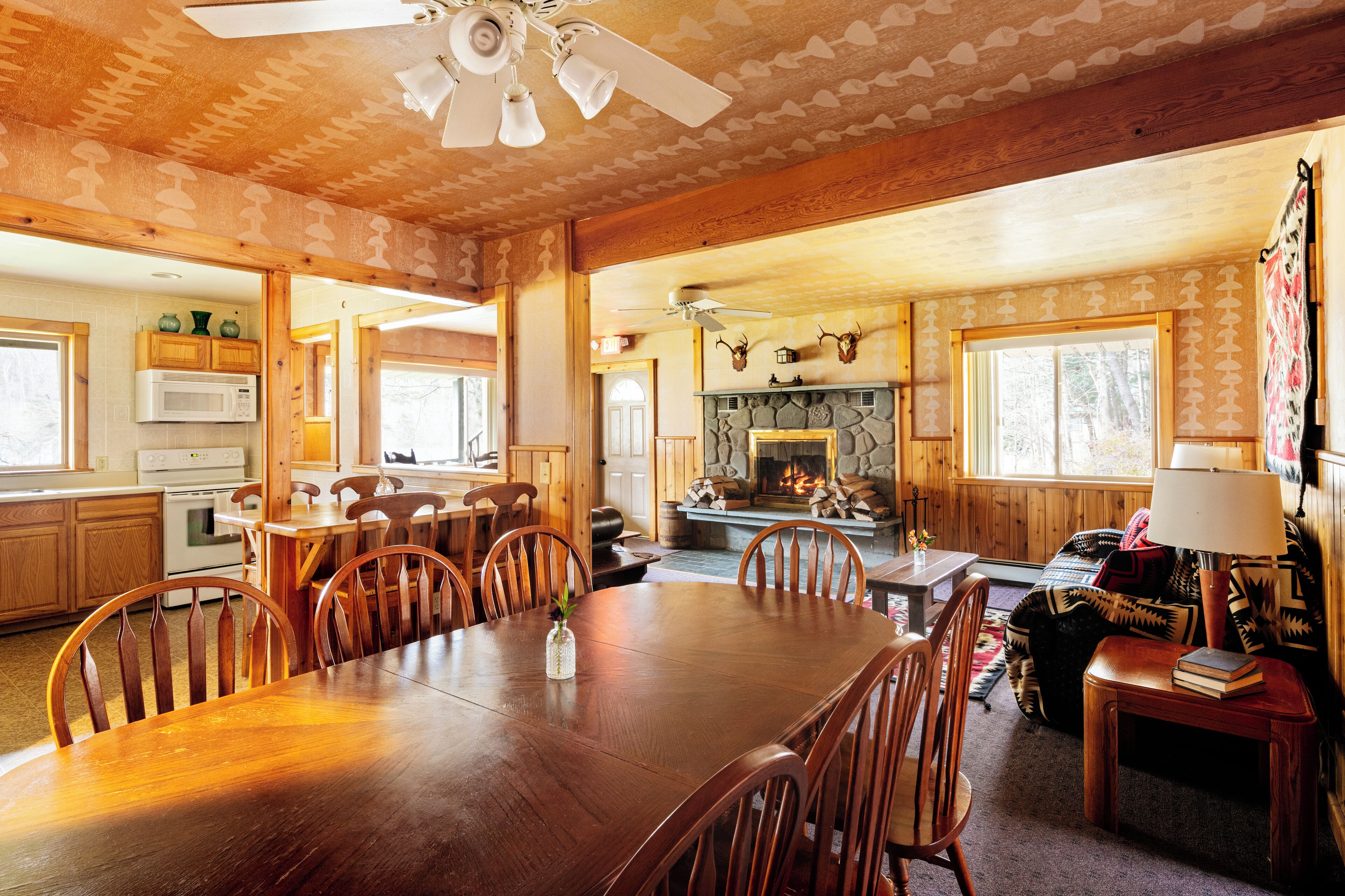 A wooden interior with a dining area, kitchen, fireplace, and a cozy seating area.