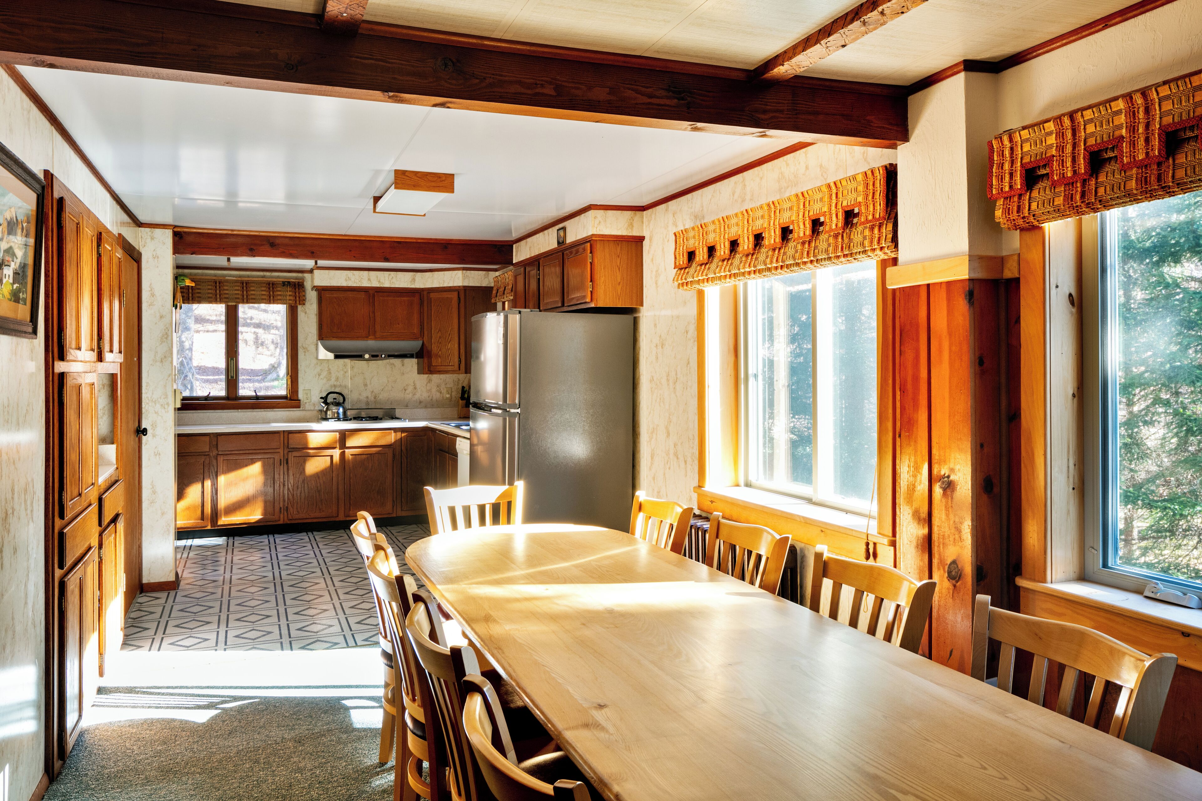 A spacious kitchen with wooden cabinets, a large dining table, and a view of the outdoors through the windows.