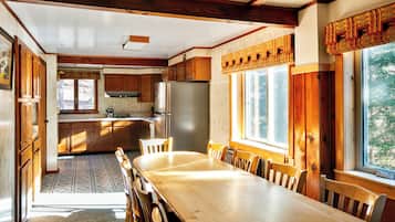 A spacious kitchen with wooden cabinets, a large dining table, and a view of the outdoors through the windows.