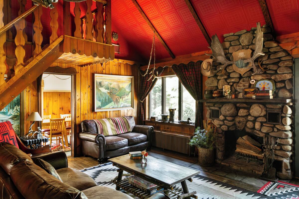 A cozy cabin interior with a stone fireplace, leather furniture, and a wooden ceiling.