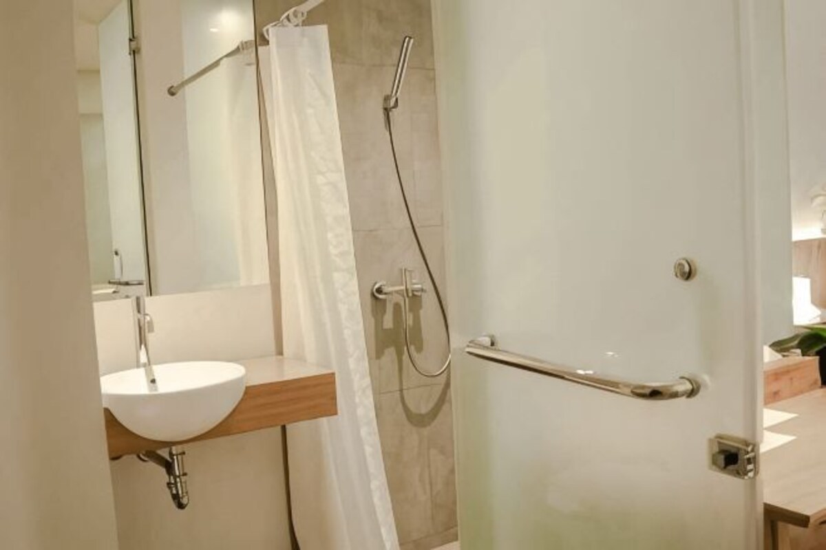 A bathroom with a sink, mirror, shower, and a door.