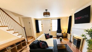 A modern living room with a sofa, a coffee table, and a fireplace. There is a staircase on the left and a flat-screen TV on the wall. - Spacious 4BR CozySuites in Old Town Alexandria (Alexandria)