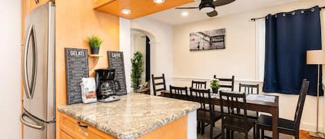A kitchen with wooden cabinets, a refrigerator, a coffee station, and a dining area with a table and chairs.