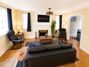 A living room with a fireplace, a sofa, a coffee table, and a television mounted above the fireplace.