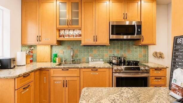 A kitchen with wooden cabinets, a stainless steel microwave, a gas stove, and a granite countertop. - Spacious 4BR CozySuites in Old Town Alexandria (Alexandria)