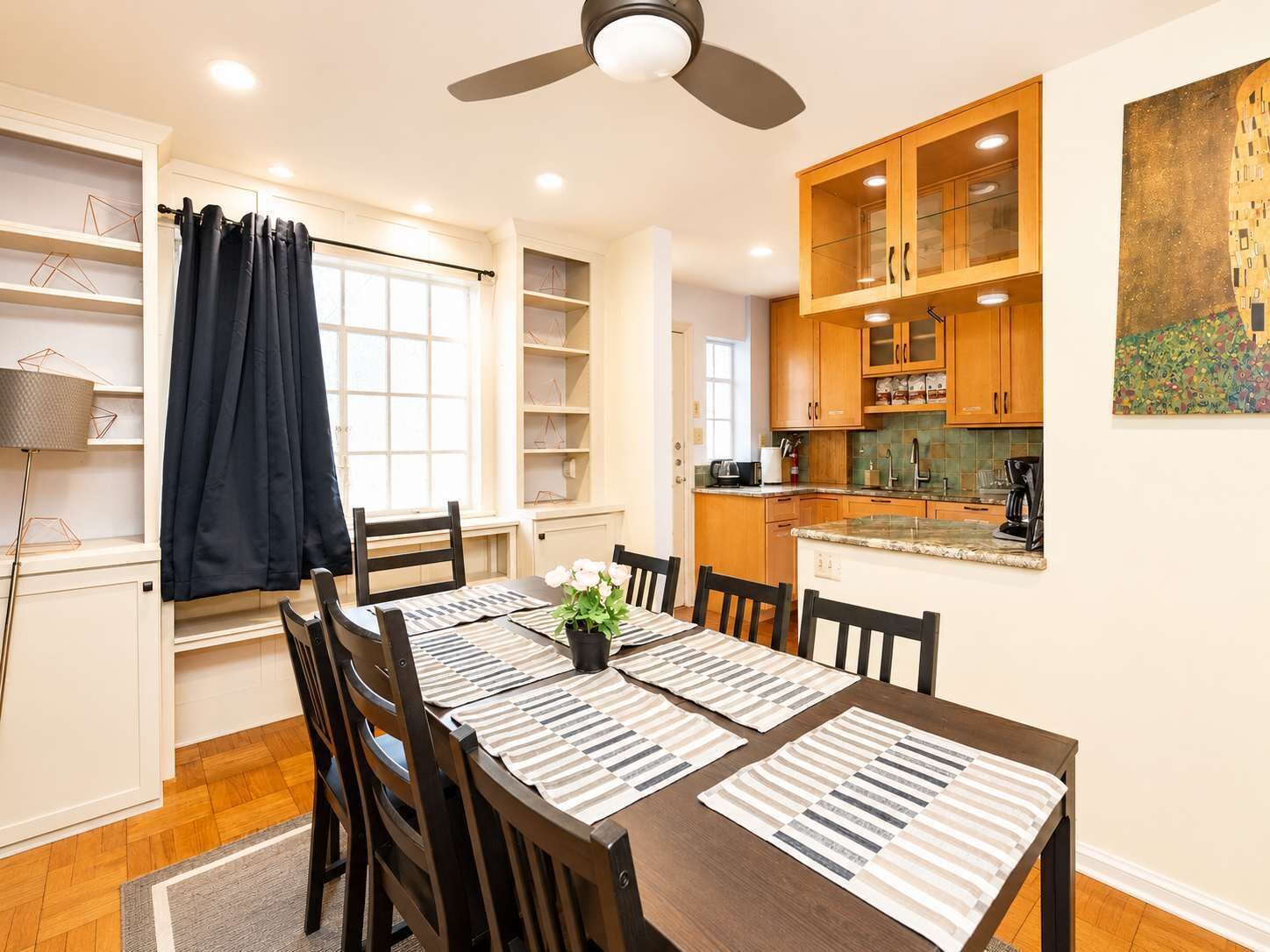 A dining area with a table set for four, surrounded by chairs, with a ceiling fan above.