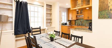 A dining area with a table set for four, surrounded by chairs, with a ceiling fan above.