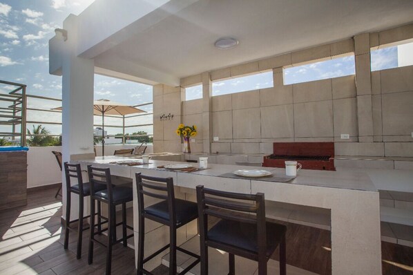 A modern outdoor kitchen with a long counter, bar stools, and a grill.
