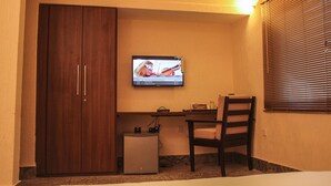 Une pièce comprenant une armoire en bois, un bureau avec un ordinateur, une chaise et un téléviseur fixé au mur.