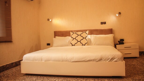 Une chambre d’hôtel avec un grand lit, une table de chevet, un climatiseur fixé au mur et une fenêtre avec des stores.