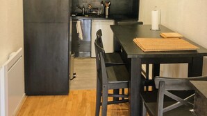 Une cuisine de taille réduite avec des meubles de rangement sombres, une table à manger en bois et un réfrigérateur.