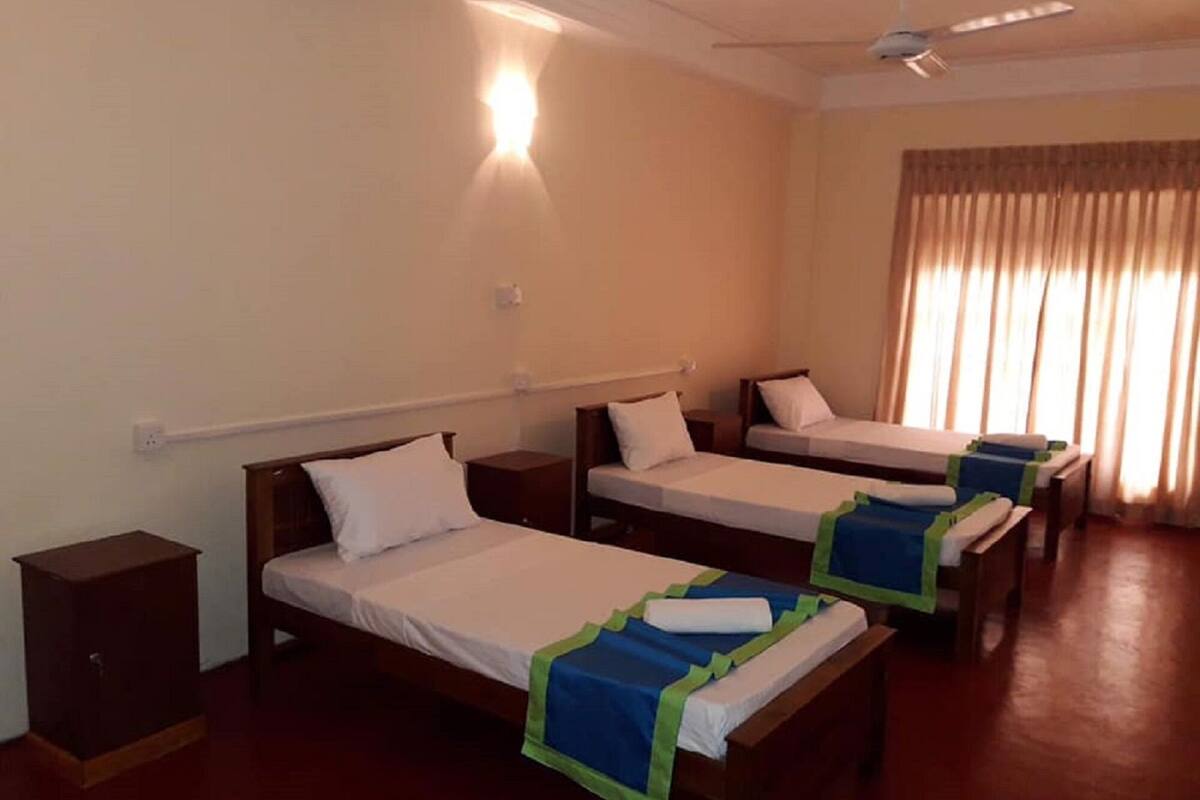 A hotel room with three single beds, a ceiling fan, and a window with curtains.