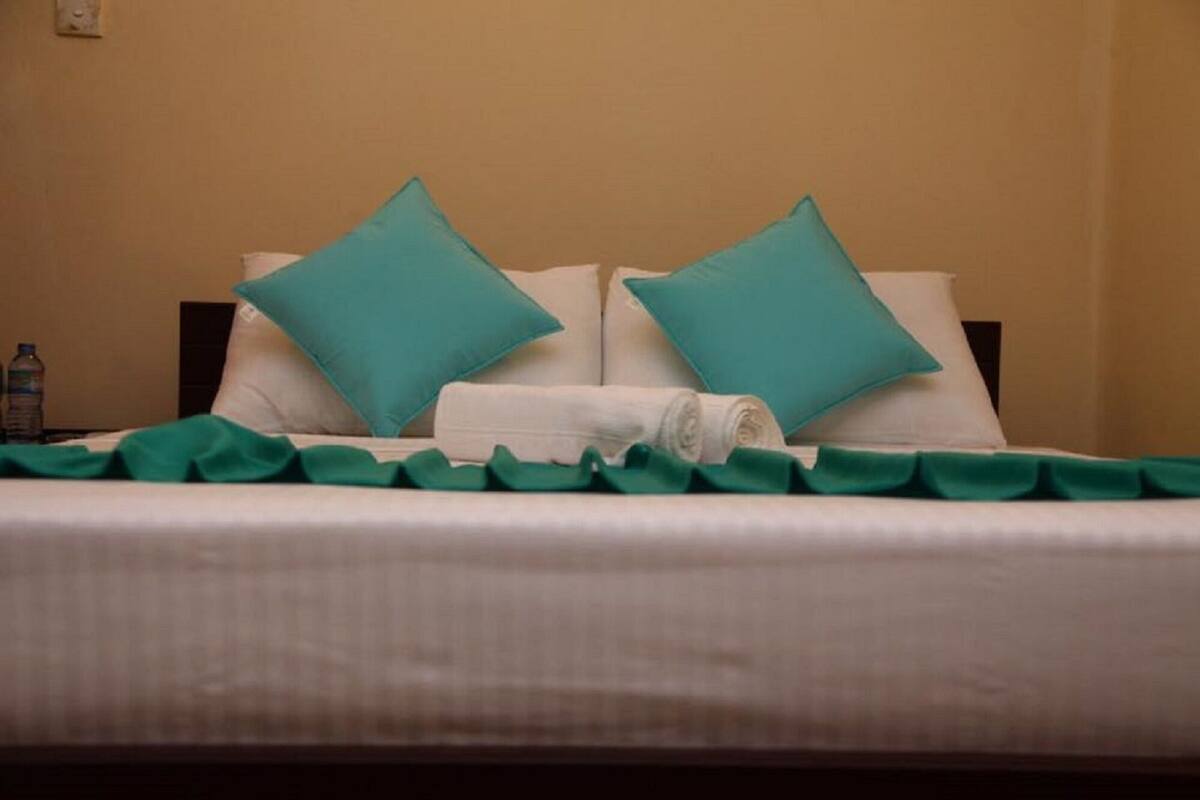 A neatly made bed with two teal pillows and a rolled white towel.