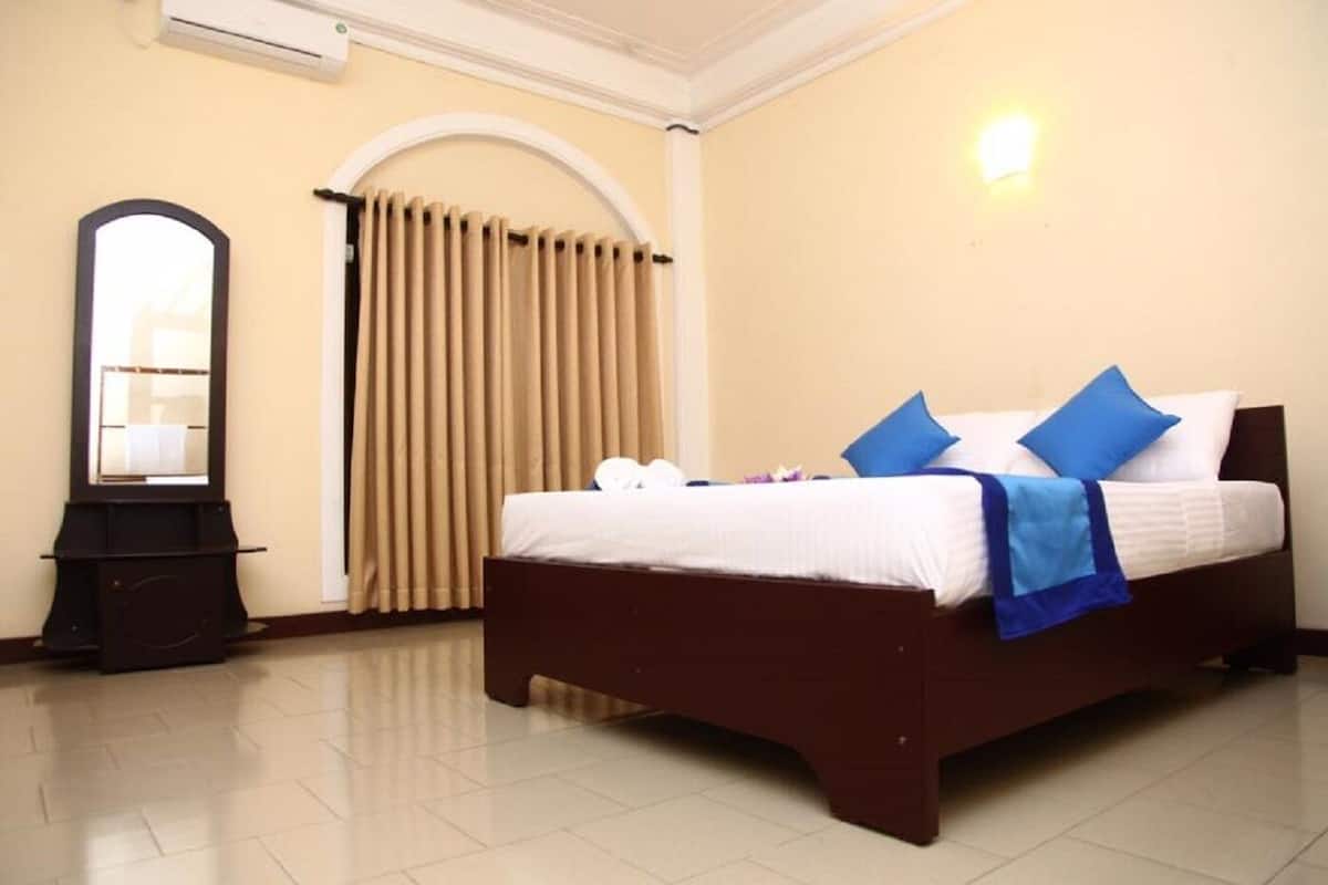 A hotel room with a bed, a mirror, a wardrobe, and a window with curtains.