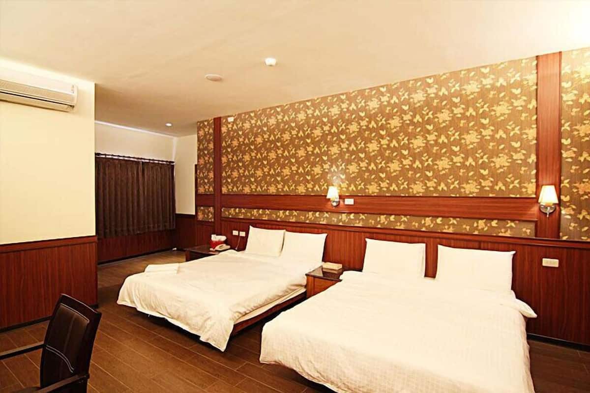 A hotel room with two beds, wooden paneling, a patterned wallpaper, and a ceiling fan.