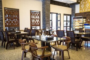 Un comedor de hotel con varias mesas y sillas, paneles decorativos y una mesa de postres.