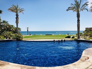 Piscina com vista para o oceano e área gramada verde.