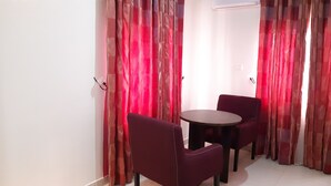 Une pièce avec une table ronde et deux chaises, des rideaux rouges et un mur blanc.
