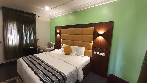 Une chambre d’hôtel avec un grand lit, une table de chevet, une chaise et un mur vert.