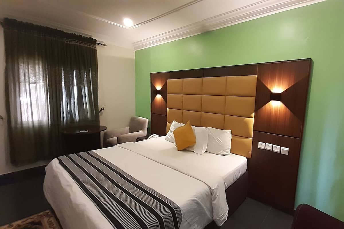 A hotel room with a large bed, a nightstand, a chair, and a green wall.