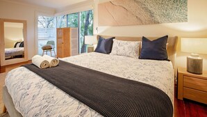 A bedroom with a large bed, a bedside table, a lamp, and a view of the outdoors.