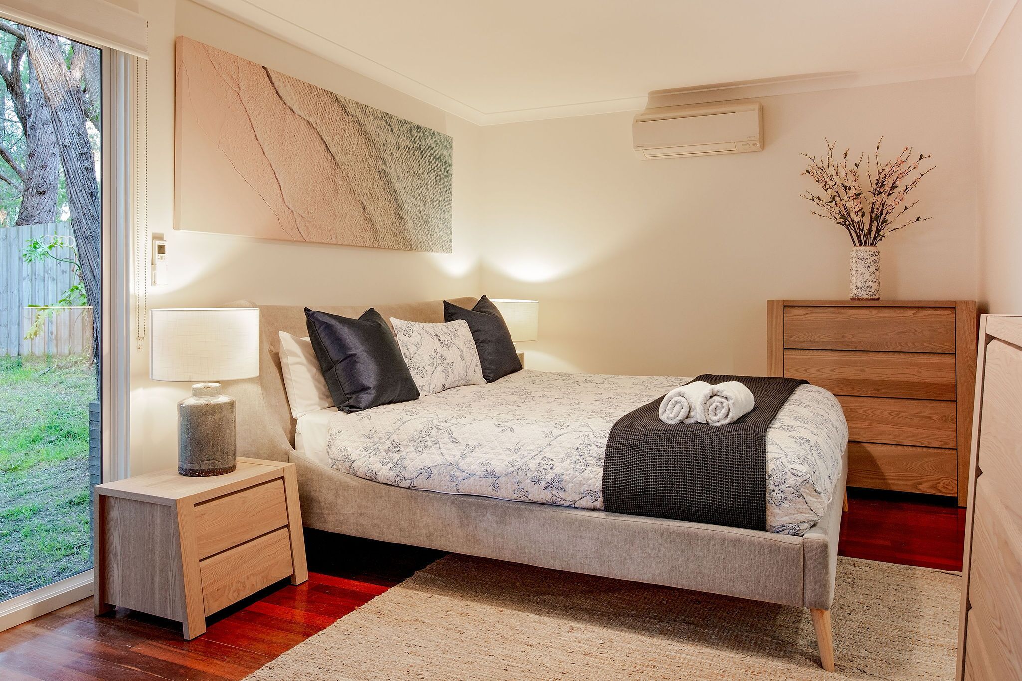 Une chambre moderne avec un lit, des tables de chevet, une commode et une grande fenêtre.
