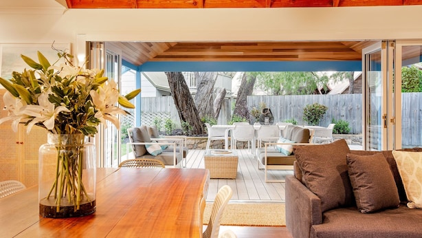 An outdoor patio area with a wooden table, white chairs, and a brown sofa.