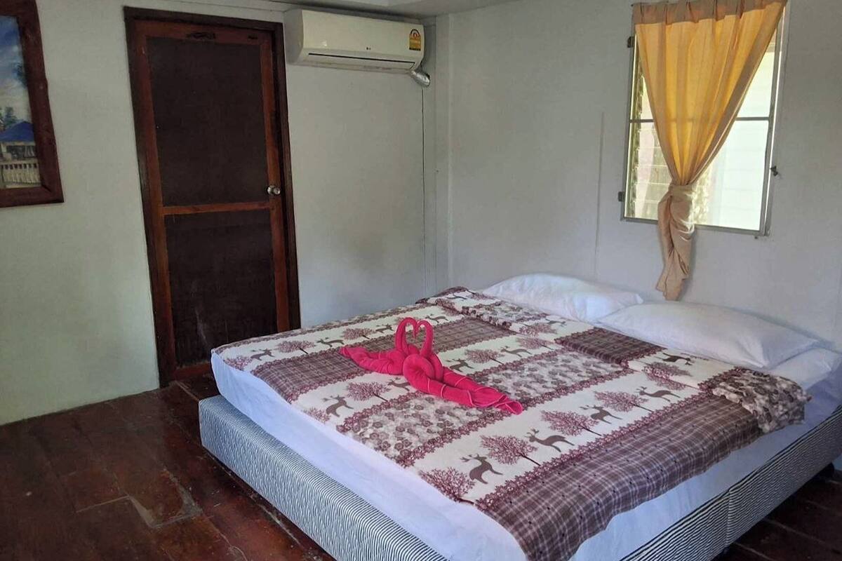 A bedroom with a bed, a door, an air conditioning unit, and a window with curtains.