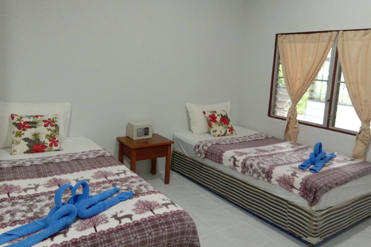 A hotel room with two beds, each with floral-patterned bedding and decorative pillows. There is a small wooden nightstand with a white radio between the beds.