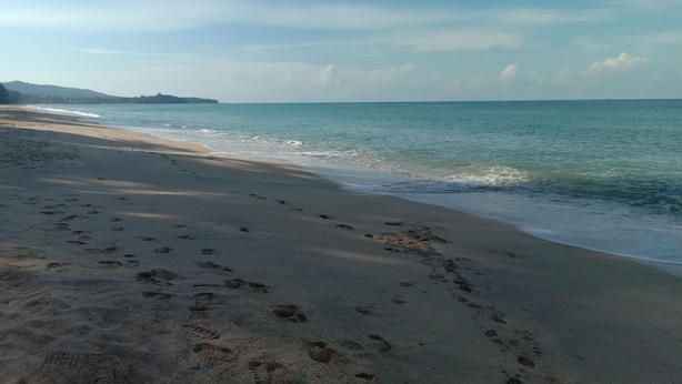 Uma praia com pegadas na areia e mar calmo.