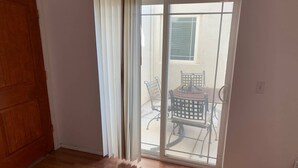 Una habitación con piso de madera, puerta corredera de vidrio que da a un patio exterior con mesa y sillas.