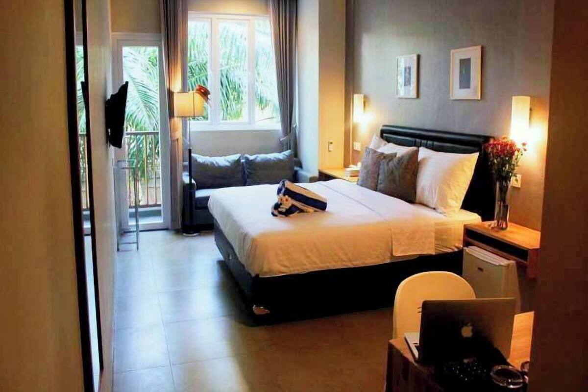 Habitación de hotel con cama, mesitas de noche, escritorio, silla, televisor y ventana con cortinas.