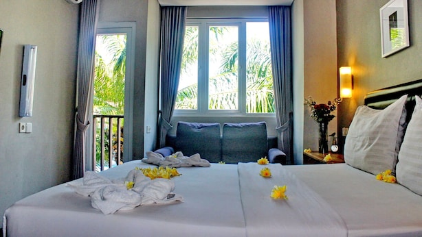 A hotel room with a bed, a nightstand, a window with curtains, and an air conditioning unit. - Kuta Beach Stay (Kuta)