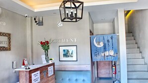 A reception area with a wooden desk, a clock, a vase with flowers, and a staircase with a blue curtain. - Kuta Beach Stay (Kuta)