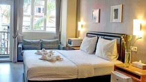 A hotel room with a large bed, a bedside table with a lamp, a TV, and a window with curtains. - Kuta Beach Stay (Kuta)