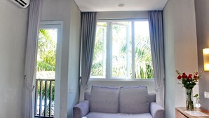A room with a grey sofa, a window with curtains, and a vase with flowers on a side table. - Kuta Beach Stay (Kuta)